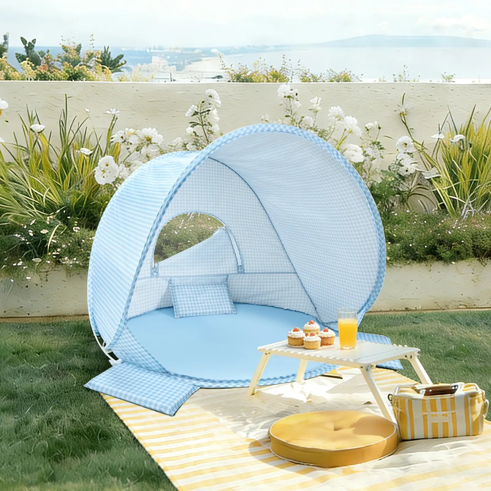 The Tiny Land® One-Stop Beach Toy & Tent Set in light blue gingham features a UV-protective tent with pillows, set on grass near a white table with snacks, plus a yellow cushion and striped mat nearby, all by a floral backdrop.|Light Blue Gingham