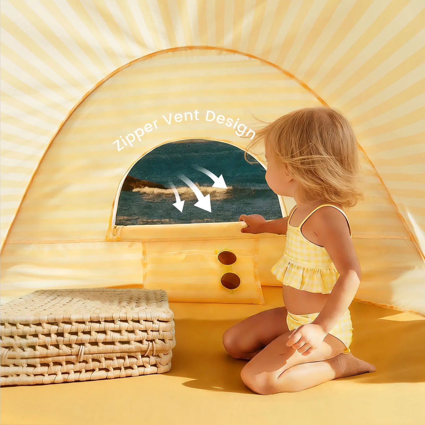 A young child sits inside the Tiny Land® One-Stop Beach Toy & Tent Set – Pastel Yellow Stripes, peering out a zippered vent toward the ocean. Arrows highlight the unique vent design. Wicker mats are stacked nearby.|Pastel Yellow Stripes