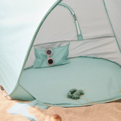 The Tiny Land® One-Stop Beach Toy & Tent Set – Sea Blue sits on the sand, complete with a matching pillow, round pink sunglasses, and a green toy turtle from Tiny Land. Some sand is scattered inside the UV-protective shade tent.|Sea Blue