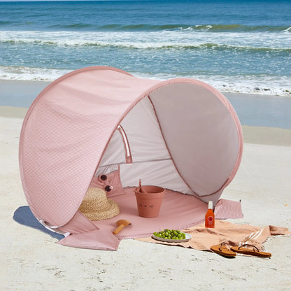 The Tiny Land® One-Stop Beach Toy & Tent Set – Blush Pink is set up by the ocean, with a straw hat, pink sunglasses, grapes, and sunscreen inside. Sandals and a bottle of sunscreen are outside, ready for sunny beach fun.|Blush Pink