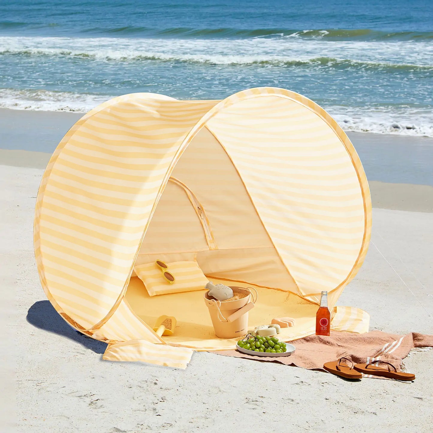 The Tiny Land® One-Stop Beach Toy & Tent Set in pastel yellow stripes keeps your towel, sandals, sunglasses, grapes, drink, woven bag, and sand play set cool and safe with UV protection by the ocean.|Pastel Yellow Stripes